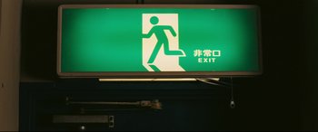 Movie still from “Ritual” (2000), directed by Hideaki Anno – A green exit sign with an image of a person going down the stairs; Extreme Close Up shot, High angle