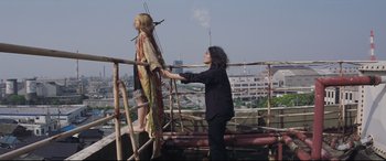 Movie still from “Ritual” (2000), directed by Hideaki Anno – A woman standing next to a man on a wooden platform; Wide shot, Low angle