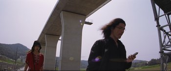 Movie still from “Ritual” (2000), directed by Hideaki Anno – A man standing next to a bridge with a sky in the background; Medium shot, Low angle