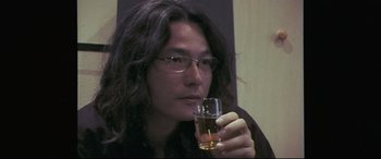 Movie still from “Ritual” (2000), directed by Hideaki Anno – A man holding a glass of alcohol in his hand; Close Up shot, High angle