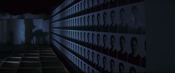 Movie still from “Ritual” (2000), directed by Hideaki Anno – A wall of pictures of a man's face in a dark room; Wide shot, High angle