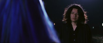 Movie still from “Ritual” (2000), directed by Hideaki Anno – A woman standing in front of a blue light at night; Close Up shot, Over the shoulder angle