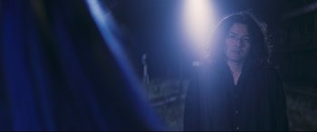 Movie still from “Ritual” (2000), directed by Hideaki Anno – A person standing in the dark with a light shining on them; Close Up shot, Over the shoulder angle
