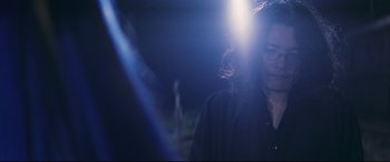 Movie still from “Ritual” (2000), directed by Hideaki Anno – A man with long hair is standing in the dark; Close Up shot, Low angle