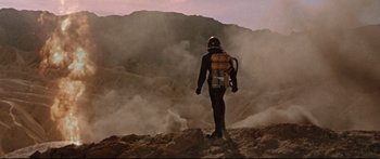 Movie still from “Robinson Crusoe on Mars” (1964), directed by Byron Haskin – A man in a full body suit walking on a rocky hill; Wide shot, Low angle