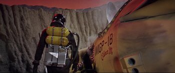 Movie still from “Robinson Crusoe on Mars” (1964), directed by Byron Haskin – A man in a helmet is standing next to an airplane; Wide shot, Low angle