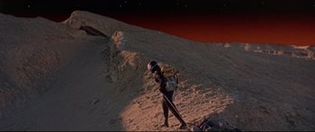 Movie still from “Robinson Crusoe on Mars” (1964), directed by Byron Haskin – A person in a spacesuit holding a stick on the side of a hill; Extreme Wide shot, High angle