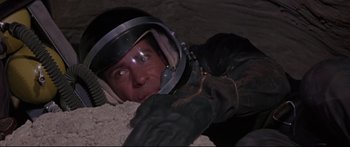 Movie still from “Robinson Crusoe on Mars” (1964), directed by Byron Haskin – A man wearing a helmet and gloves laying on a pile of dirt; Close Up shot, Overhead angle