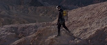 Movie still from “Robinson Crusoe on Mars” (1964), directed by Byron Haskin – A man in a black suit and helmet walking on a rocky hill; Wide shot, High angle