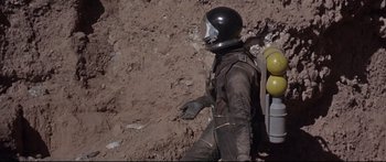 Movie still from “Robinson Crusoe on Mars” (1964), directed by Byron Haskin – A man in a space suit is walking in the dirt; Wide shot, Low angle