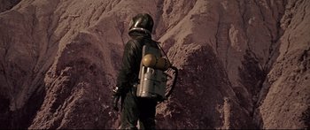 Movie still from “Robinson Crusoe on Mars” (1964), directed by Byron Haskin – A man in a space suit with a helmet on his back; Wide shot, Low angle