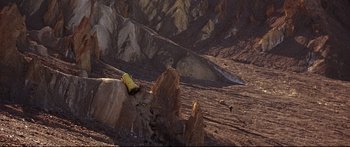 Movie still from “Robinson Crusoe on Mars” (1964), directed by Byron Haskin – A yellow bottle sitting on the side of a mountain; Extreme Wide shot, Overhead angle