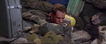 Movie still from “Robinson Crusoe on Mars” (1964), directed by Byron Haskin – A man in a scuba diving suit is laying on the rocks; Medium shot, High angle