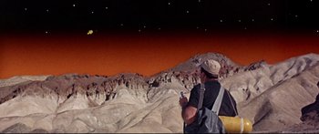Movie still from “Robinson Crusoe on Mars” (1964), directed by Byron Haskin – A man standing on top of a mountain holding a cell phone; Extreme Wide shot, Low angle