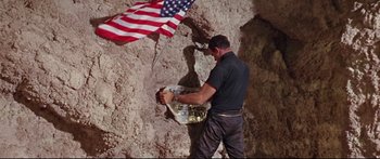 Movie still from “Robinson Crusoe on Mars” (1964), directed by Byron Haskin – A man working on a wall with an american flag hanging from a pole; Medium shot, Low angle