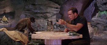 Movie still from “Robinson Crusoe on Mars” (1964), directed by Byron Haskin – A man sitting at a table with a monkey sitting at the table; Medium shot, Over the shoulder angle