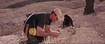 Movie still from “Robinson Crusoe on Mars” (1964), directed by Byron Haskin – A man sitting on the ground looking at his cell phone; Medium shot, High angle