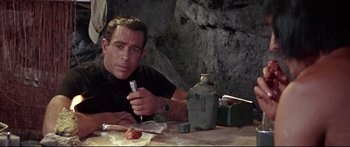 Movie still from “Robinson Crusoe on Mars” (1964), directed by Byron Haskin – A man sitting at a table holding a bottle of water; Close Up shot, High angle