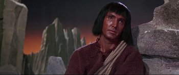Movie still from “Robinson Crusoe on Mars” (1964), directed by Byron Haskin – A man with long black hair wearing a brown shirt; Close Up shot, Over the shoulder angle