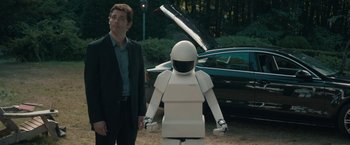 Movie still from “Robot & Frank” (2012), directed by Jake Schreier – A man standing next to a robot in front of a car; Wide shot, Over the shoulder angle
