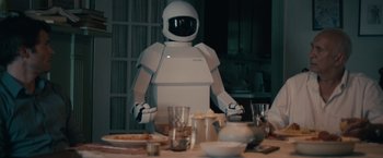 Movie still from “Robot & Frank” (2012), directed by Jake Schreier – A robot standing in front of a dinner table; Medium shot, Over the shoulder angle