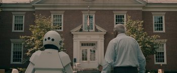 Movie still from “Robot & Frank” (2012), directed by Jake Schreier – Two people standing in front of a building with a flag; Wide shot, Over the shoulder angle