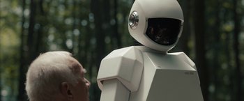 An old man looking at a robot in a forest