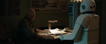 Movie still from “Robot & Frank” (2012), directed by Jake Schreier – A man sitting at a table with papers and a lamp; Medium shot, Low angle