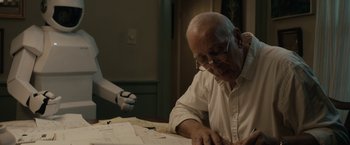 Movie still from “Robot & Frank” (2012), directed by Jake Schreier – An old man sitting at a table writing on a piece of paper; Medium shot, Over the shoulder angle