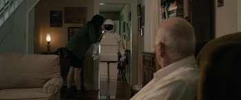 Movie still from “Robot & Frank” (2012), directed by Jake Schreier – A woman standing in front of a robot in a living room; Medium shot, Over the shoulder angle