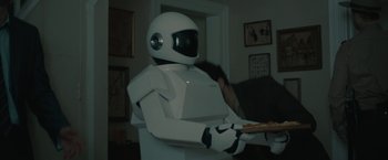 Movie still from “Robot & Frank” (2012), directed by Jake Schreier – A white robot sitting on top of a table holding a pizza; Medium shot, Over the shoulder angle