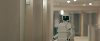 Movie still from “Robot & Frank” (2012), directed by Jake Schreier – A white robot standing in front of a white wall; Wide shot, Low angle