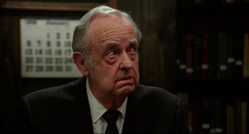 Movie still from “Rock 'n' Roll High School” (1979), directed by Joe Dante – An older man in a suit and tie looking at the camera; Close Up shot, Over the shoulder angle