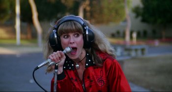 Movie still from “Rock 'n' Roll High School” (1979), directed by Joe Dante – A woman wearing headphones and singing into a microphone; Medium shot, Low angle