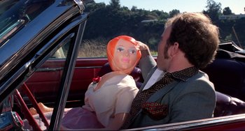 Movie still from “Rock 'n' Roll High School” (1979), directed by Joe Dante – A man sitting in the back seat of a car with a mannequin head; Medium shot, Over the shoulder angle