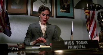 Movie still from “Rock 'n' Roll High School” (1979), directed by Joe Dante – A woman sitting at a desk in front of a sign; Medium shot, Low angle