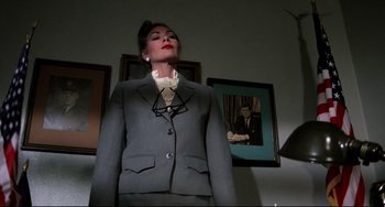Movie still from “Rock 'n' Roll High School” (1979), directed by Joe Dante – A woman in a suit and tie standing in front of a picture; Medium shot, Low angle