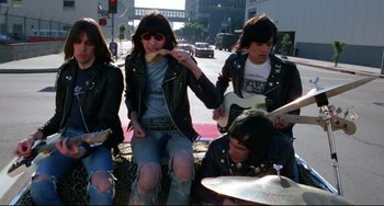 Movie still from “Rock 'n' Roll High School” (1979), directed by Joe Dante – A group of people sitting on the side of a road; Medium shot, Low angle