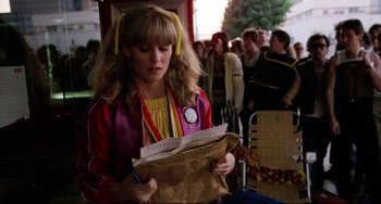 Movie still from “Rock 'n' Roll High School” (1979), directed by Joe Dante – A woman holding a paper bag while standing in a crowd; Medium shot, Over the shoulder angle