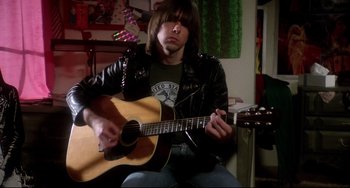Movie still from “Rock 'n' Roll High School” (1979), directed by Joe Dante – A man sitting down while playing an acoustic guitar; Medium shot, Low angle