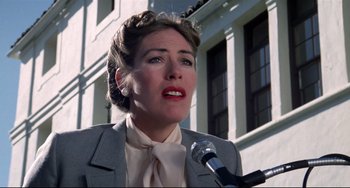 Movie still from “Rock 'n' Roll High School” (1979), directed by Joe Dante – A woman in a gray suit is speaking into a microphone; Close Up shot, Low angle