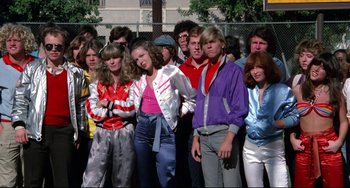 Movie still from “Rock 'n' Roll High School” (1979), directed by Joe Dante – A group of people standing next to each other in front of a fence; Medium shot, High angle