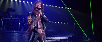 Movie still from “Rock Star” (2001), directed by Stephen Herek – A man in a leather jacket singing into a microphone; Medium shot, Low angle