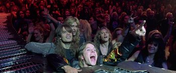 Movie still from “Rock Star” (2001), directed by Stephen Herek – A group of people sitting in front of an audience; Medium shot, Low angle