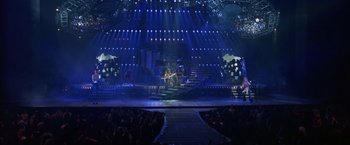 Movie still from “Rock Star” (2001), directed by Stephen Herek – A group of people on a stage with lights in the background; Extreme Wide shot, High angle