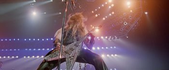 Movie still from “Rock Star” (2001), directed by Stephen Herek – A man with long blond hair is holding a guitar; Wide shot, High angle