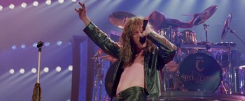 Movie still from “Rock Star” (2001), directed by Stephen Herek – A man in a leather jacket is holding a microphone; Medium shot, Low angle