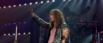 Movie still from “Rock Star” (2001), directed by Stephen Herek – A man in a leather jacket waves to the crowd; Medium shot, Low angle