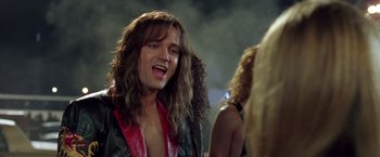 Movie still from “Rock Star” (2001), directed by Stephen Herek – A man with long brown hair and a red shirt; Close Up shot, Low angle
