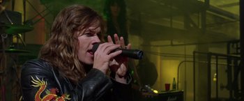 Movie still from “Rock Star” (2001), directed by Stephen Herek – A man in a leather jacket is singing into a microphone; Close Up shot, Low angle